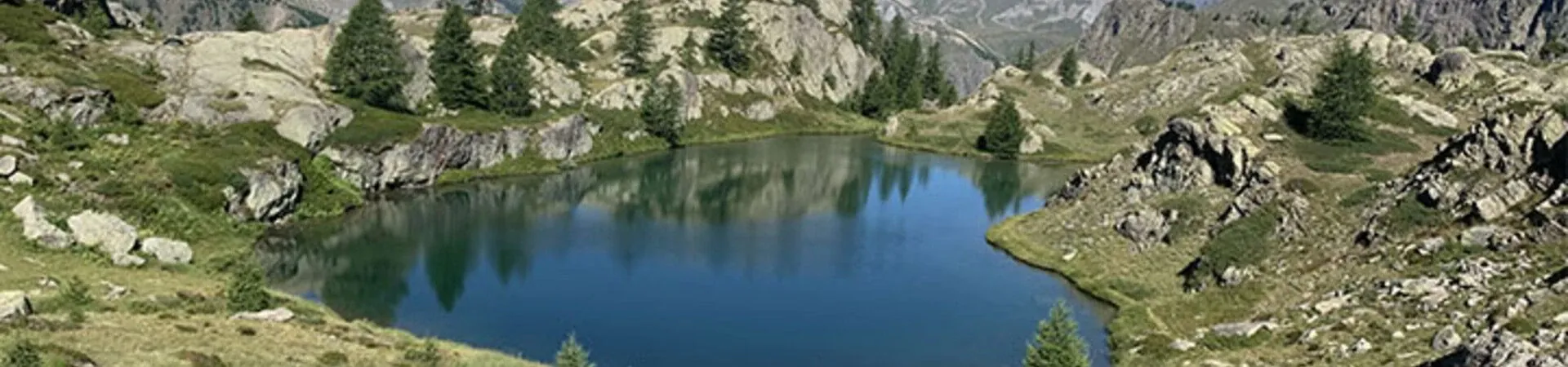 Lac alpin entoure de rochers et sapins - Grande Traversee des Alpes France