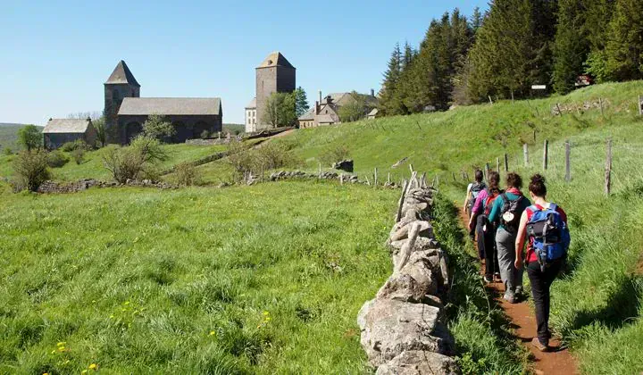 Randonneurs sur sentier vers un village medieval - Aubrac France