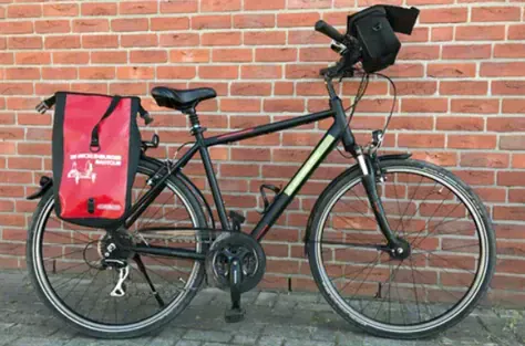 Velo de tourisme homme avec sacoche rouge devant mur de briques - Cote Baltique Allemagne